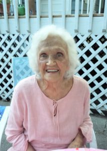 An older woman in a pink shirt sitting at a table.