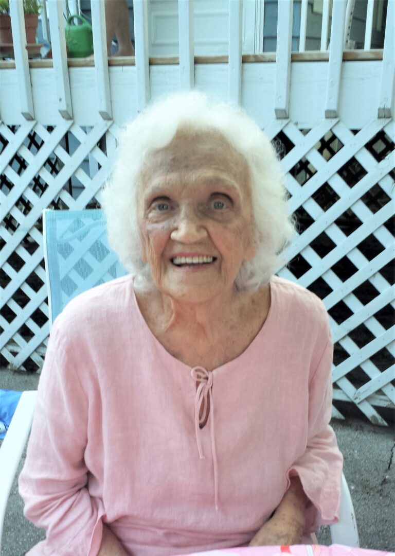 An older woman in a pink shirt sitting at a table.