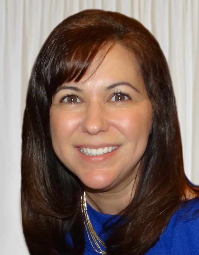 A woman in a blue top smiling for the camera.