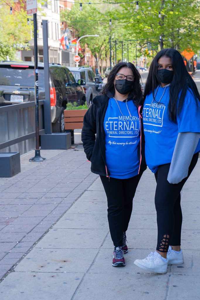 Two women in blue t - shirts standing on a sidewalk.