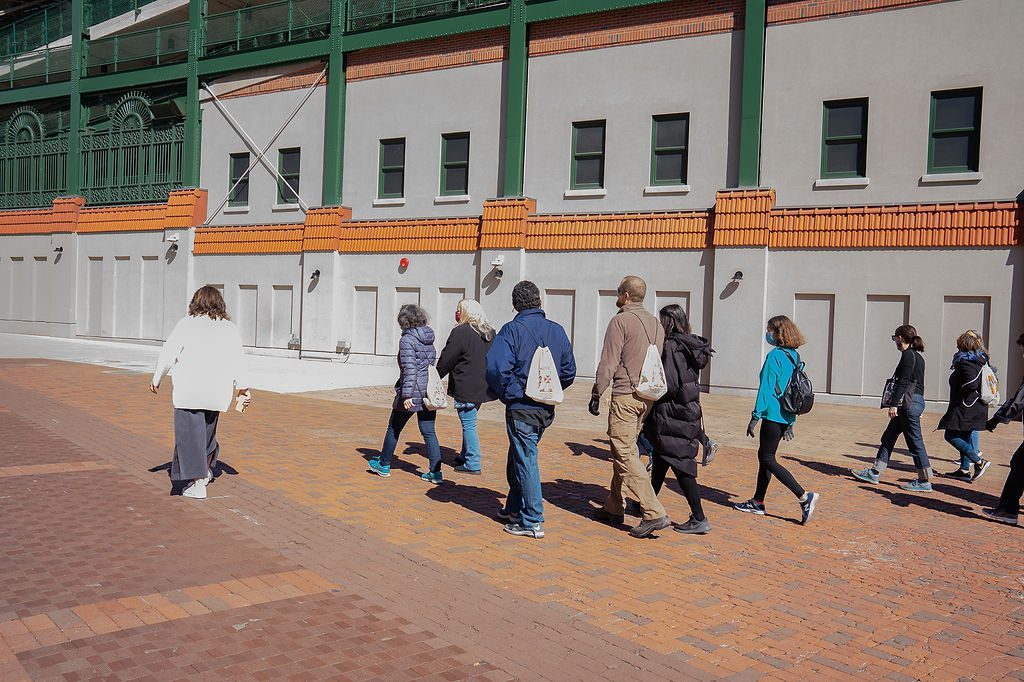 A group of people walking in front of a baseball stadium.