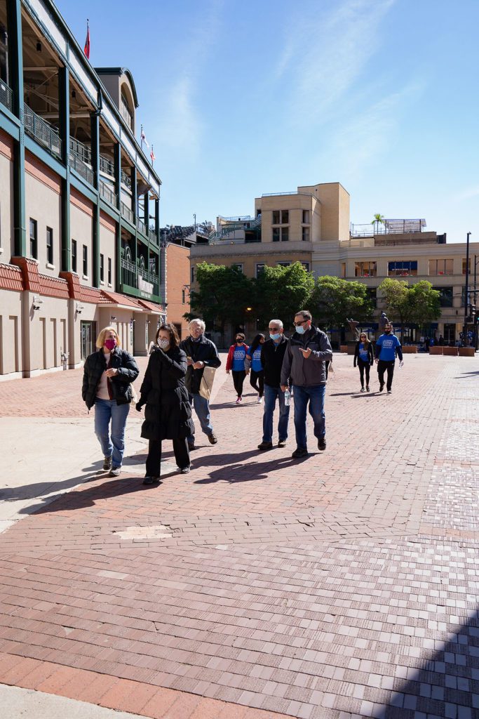 A group of people walking down a brick sidewalk in front of a baseball stadium.