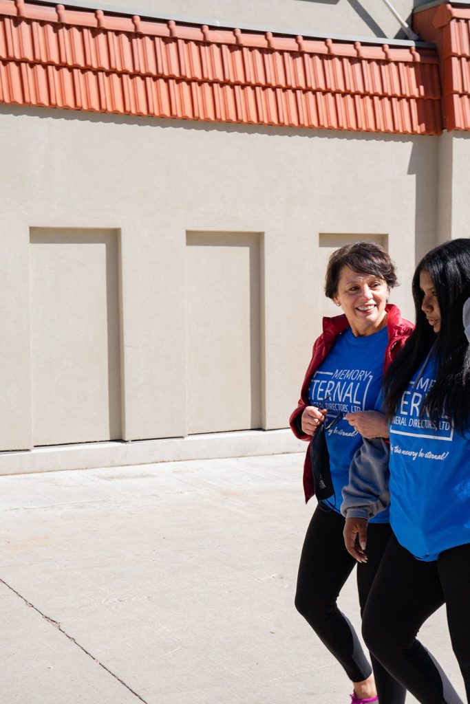 Two women in blue t - shirts walking in front of a building.