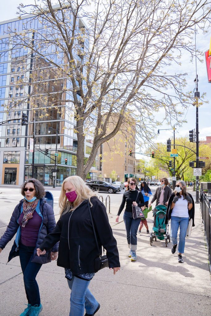 A group of people walking down a sidewalk with masks on.