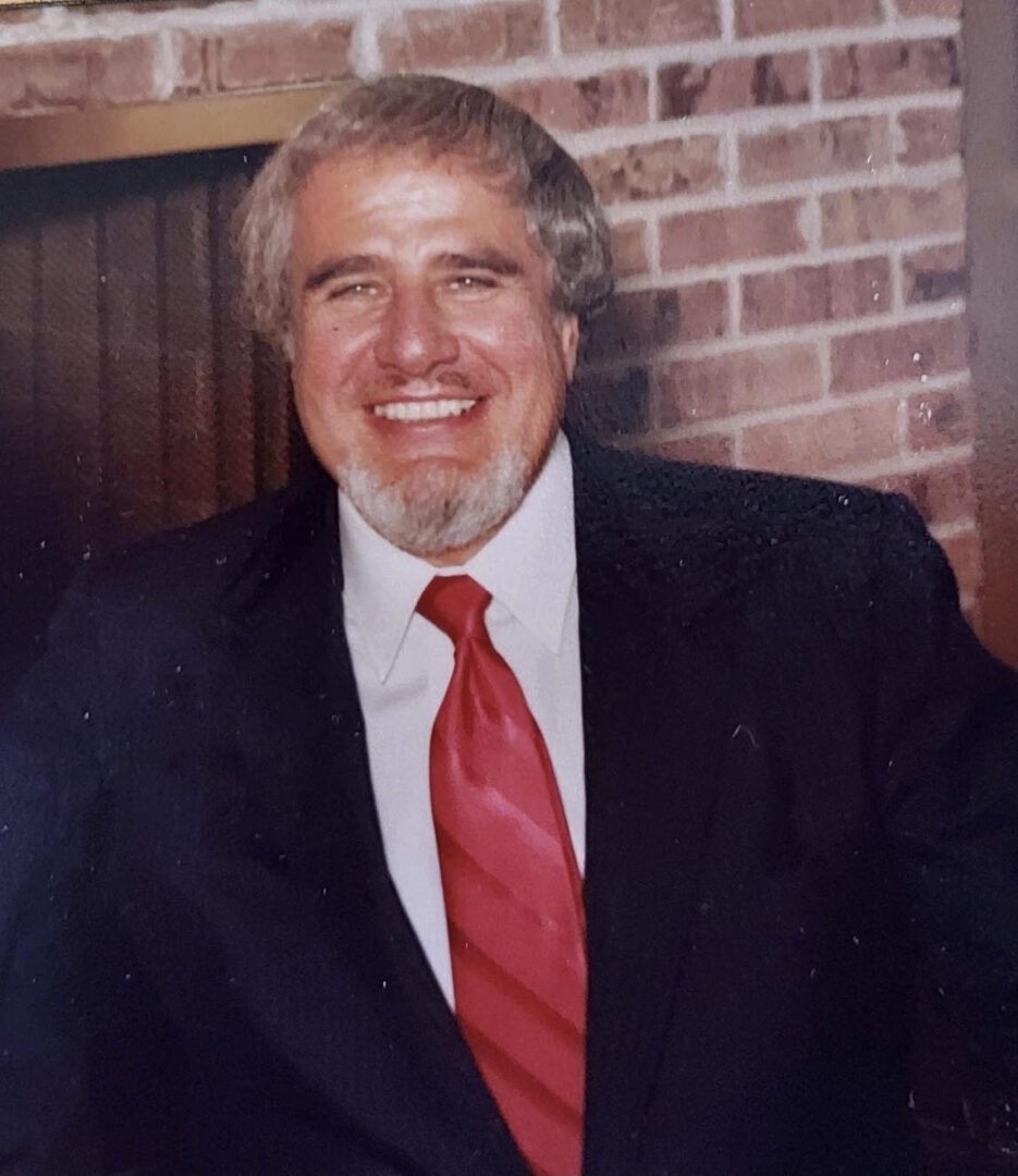 A man in a suit and tie smiling in front of a brick fireplace.