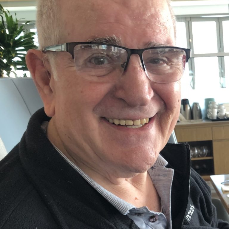 An older man with glasses smiling at a table.