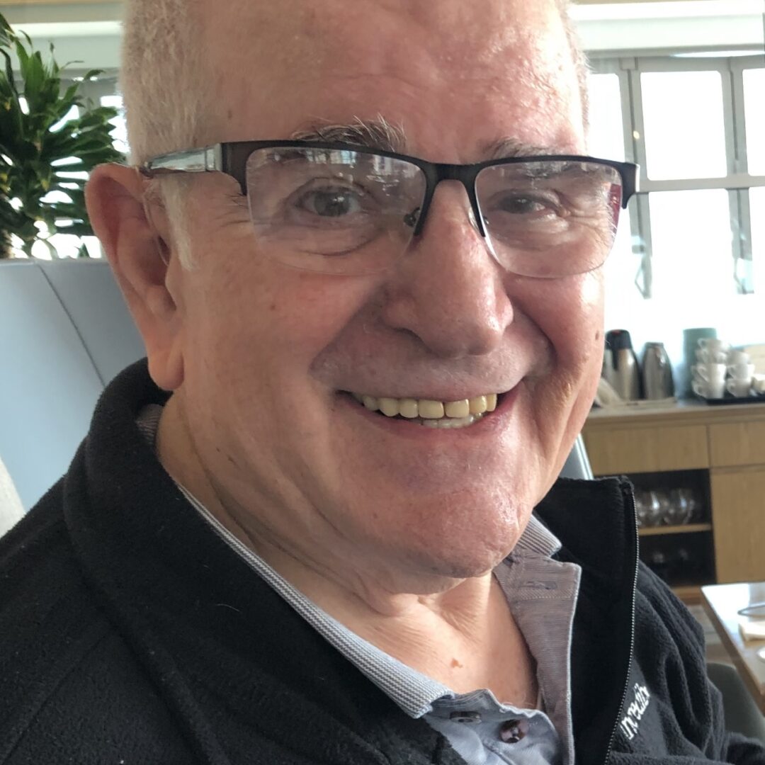 An older man with glasses smiling at a table.