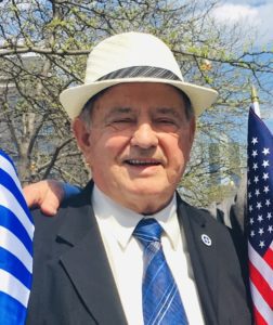 Two men in suits and hats standing next to two american and greek flags.