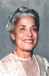 An older woman wearing a white dress and pearls.