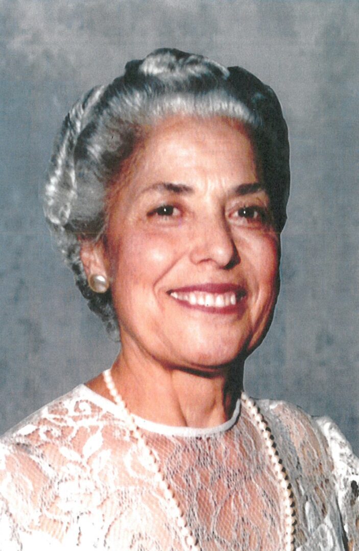 An older woman wearing a white dress and pearls.