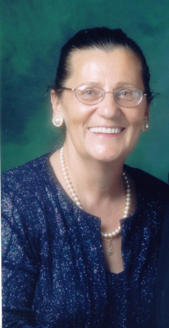 A woman with glasses and pearls smiling for the camera.