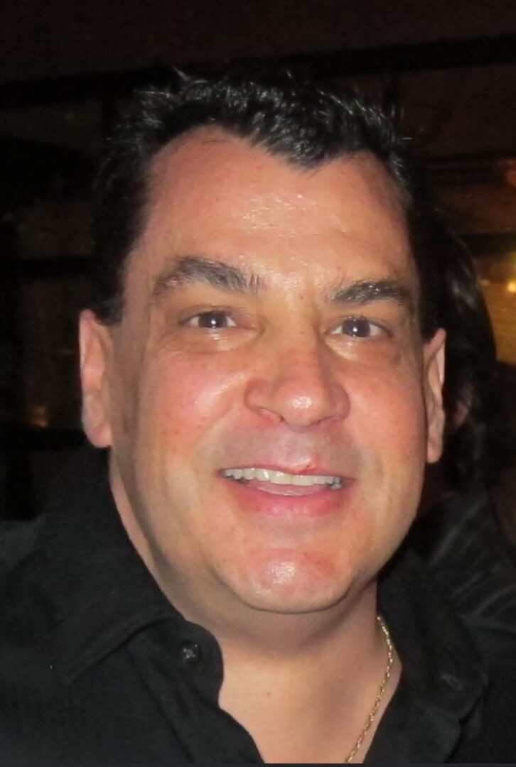 A man in a black shirt smiling for the camera.