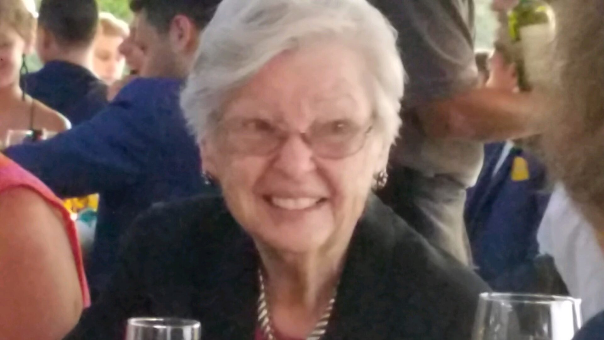 An older woman smiles while sitting at a table.
