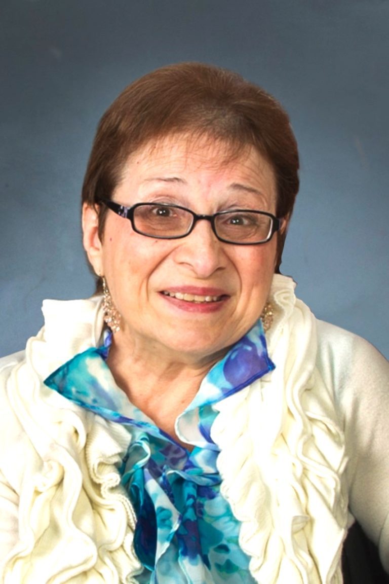 An older woman wearing glasses and a ruffled shirt.