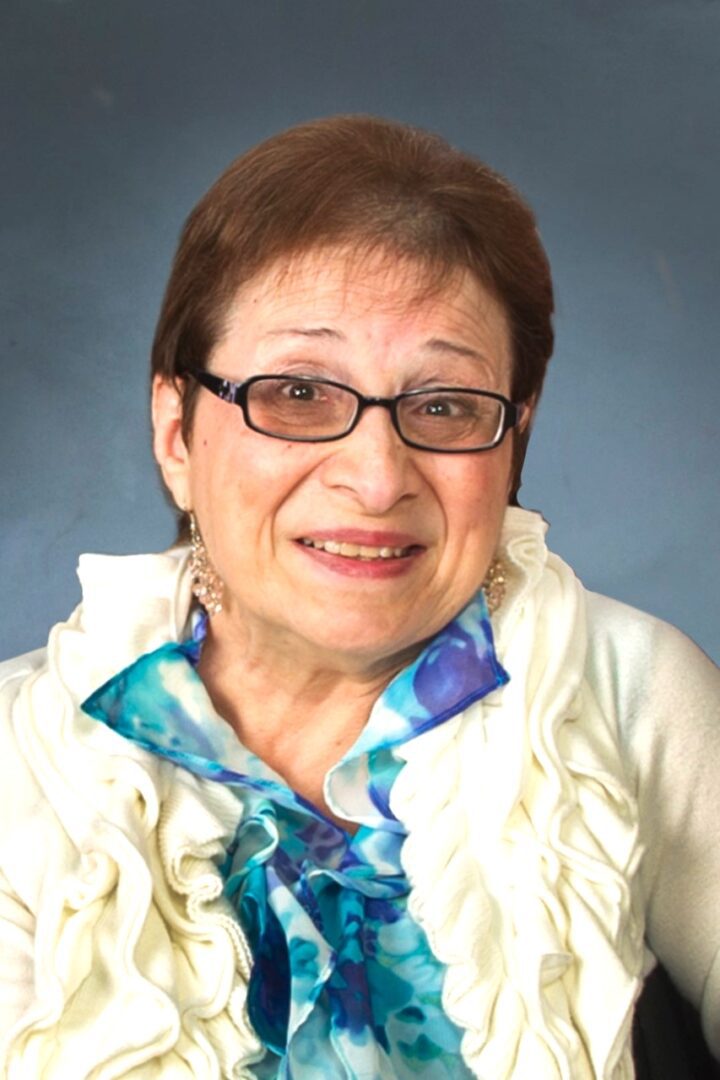 An older woman wearing glasses and a ruffled shirt.