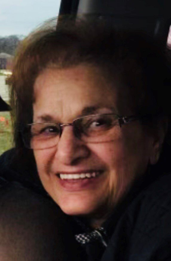 An older woman smiling in the back seat of a car.