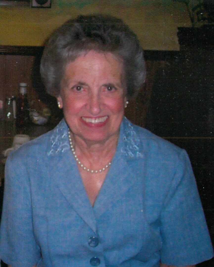 An older woman wearing a blue dress and pearls.