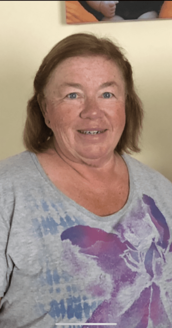 A woman in a grey t - shirt smiles in front of a picture.