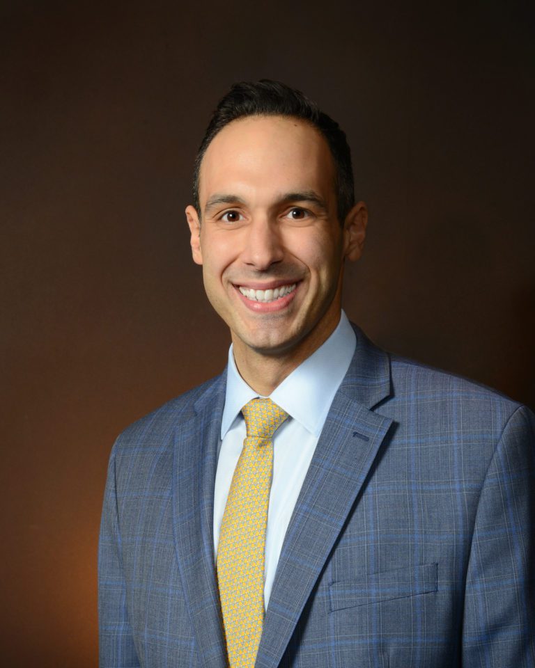 A smiling man in a suit and yellow tie.