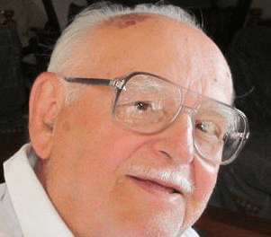 An older man wearing glasses and a white shirt.