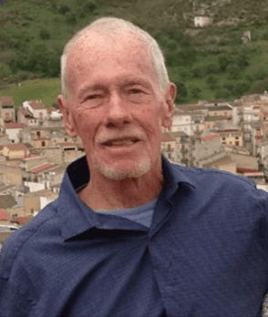 An older man standing in front of a town.