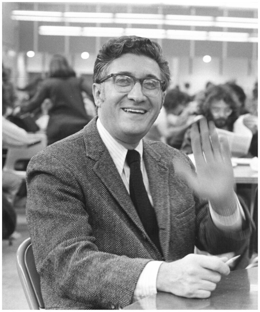 A black and white photo of a man waving at a table.