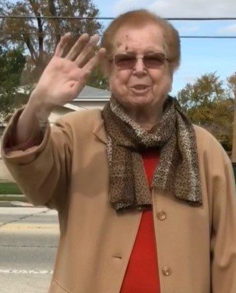 An older woman is waving in the street.
