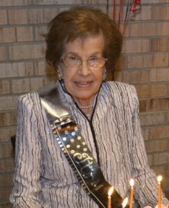 A woman sitting in front of a birthday cake.