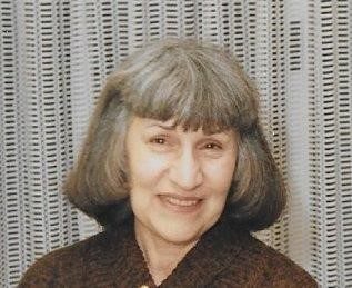 A woman in a brown sweater smiles in front of a curtain.