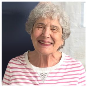 An older woman smiling in a pink and white striped shirt.