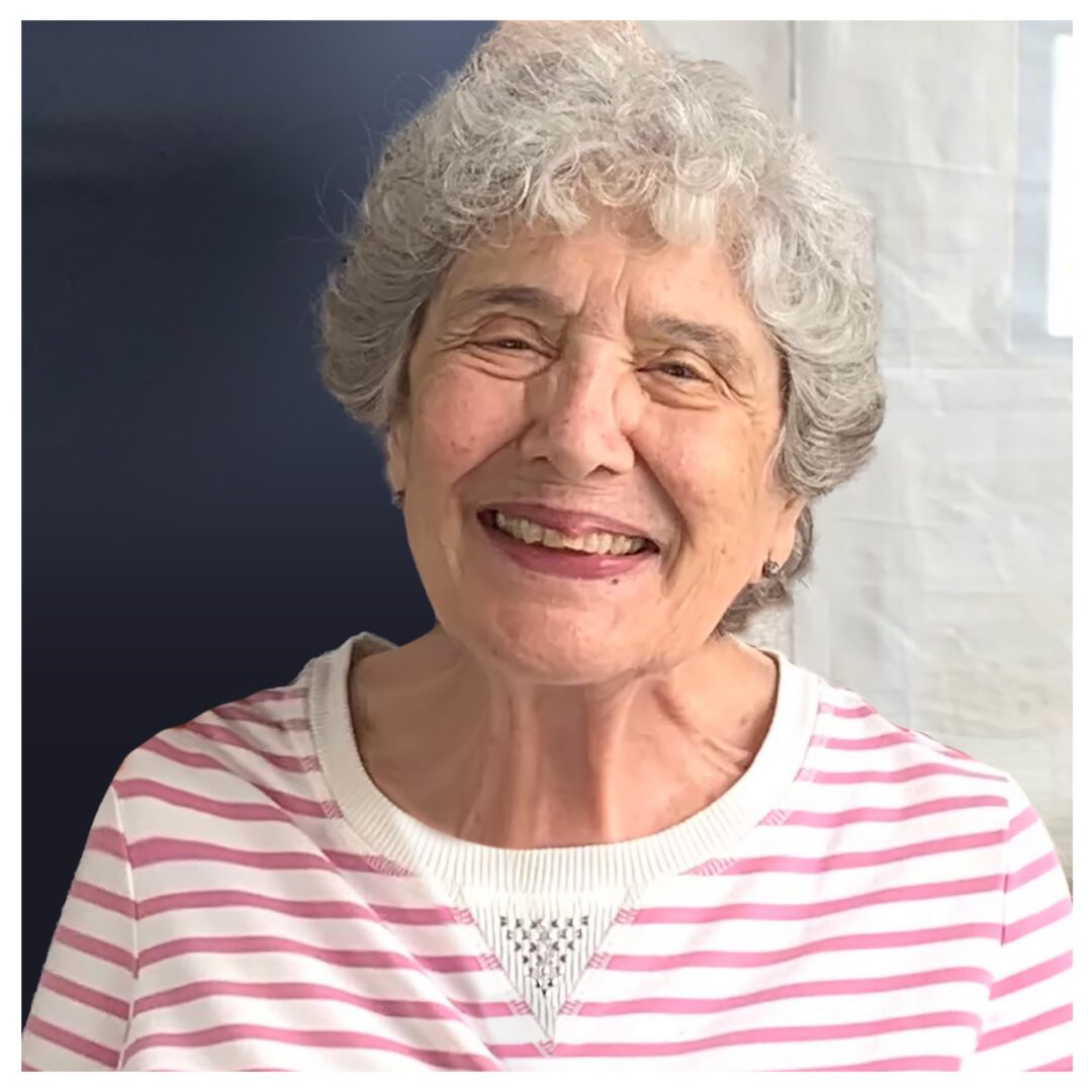 An older woman smiling in a pink and white striped shirt.
