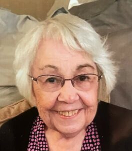 An older woman with glasses smiles for the camera.