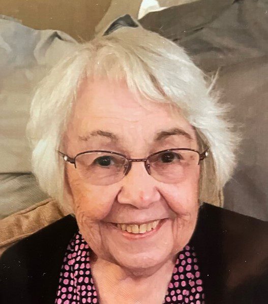 An older woman with glasses smiles for the camera.