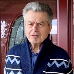 A man in a blue and white sweater standing in front of a door.
