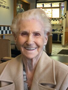 An older woman smiling in front of a restaurant.