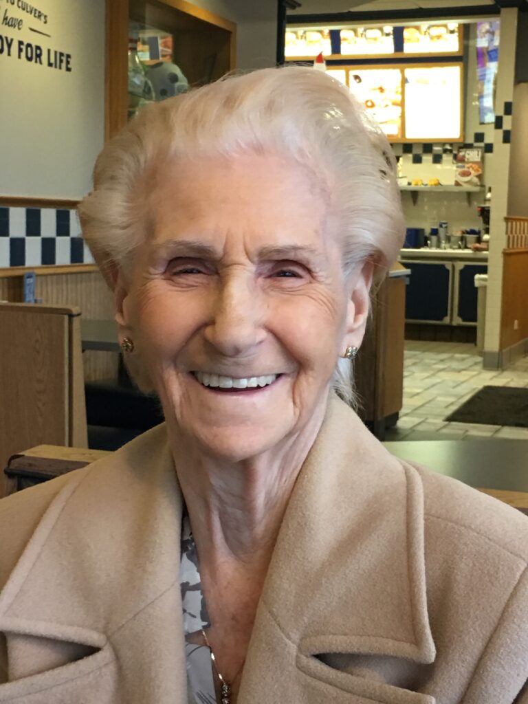 An older woman smiling in front of a restaurant.