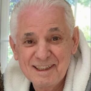 An older man in a towel smiles for the camera.