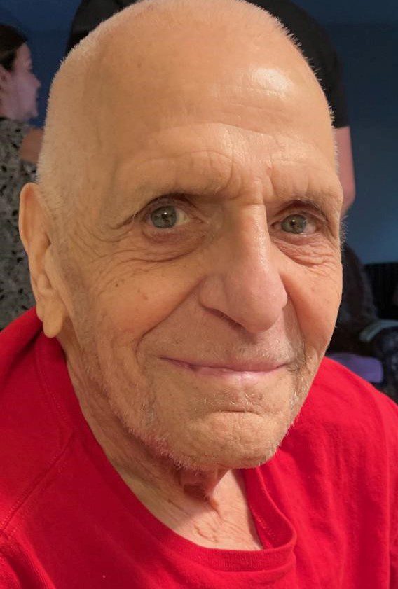 An older man in a red shirt smiles for the camera.