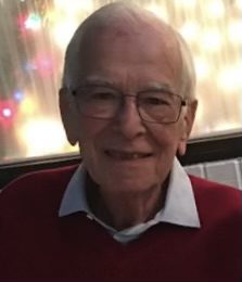An older man in a red sweater smiles for the camera.