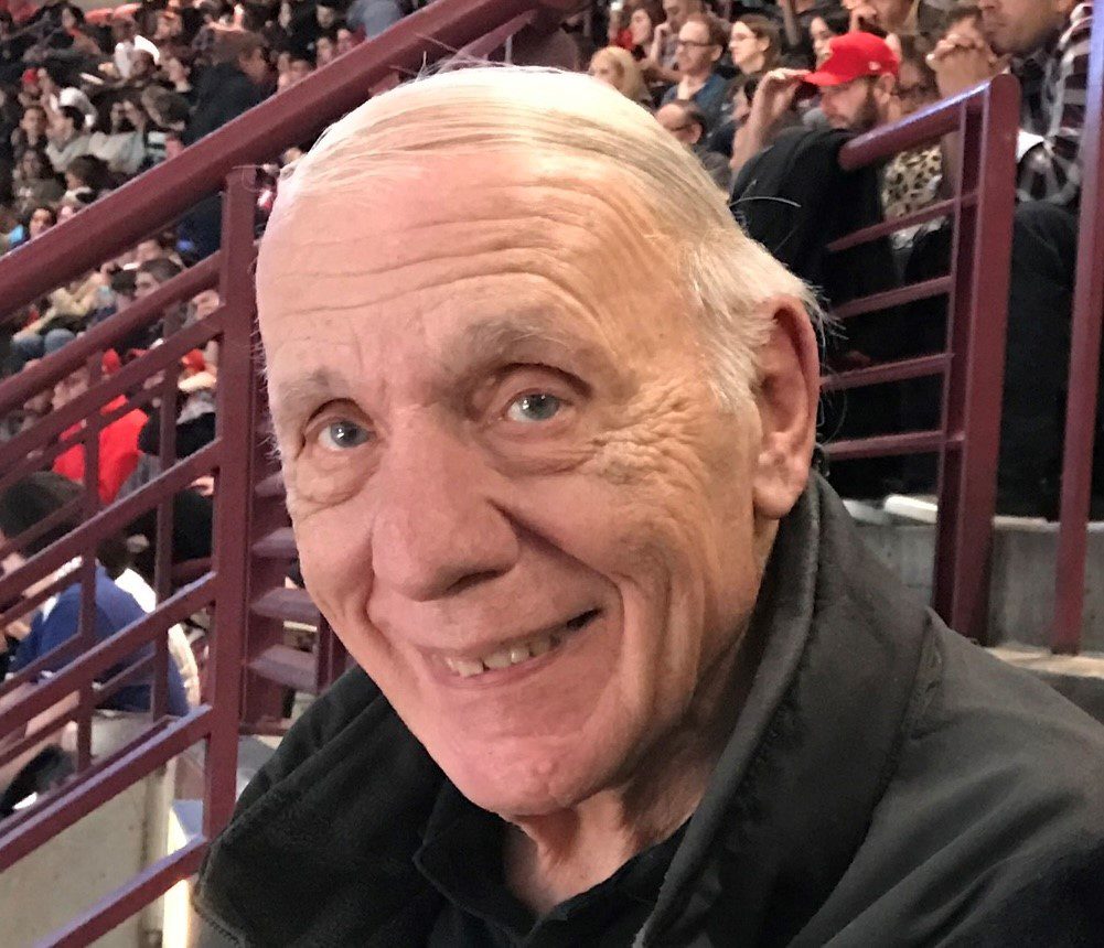 An older man sitting in the stands at a hockey game.