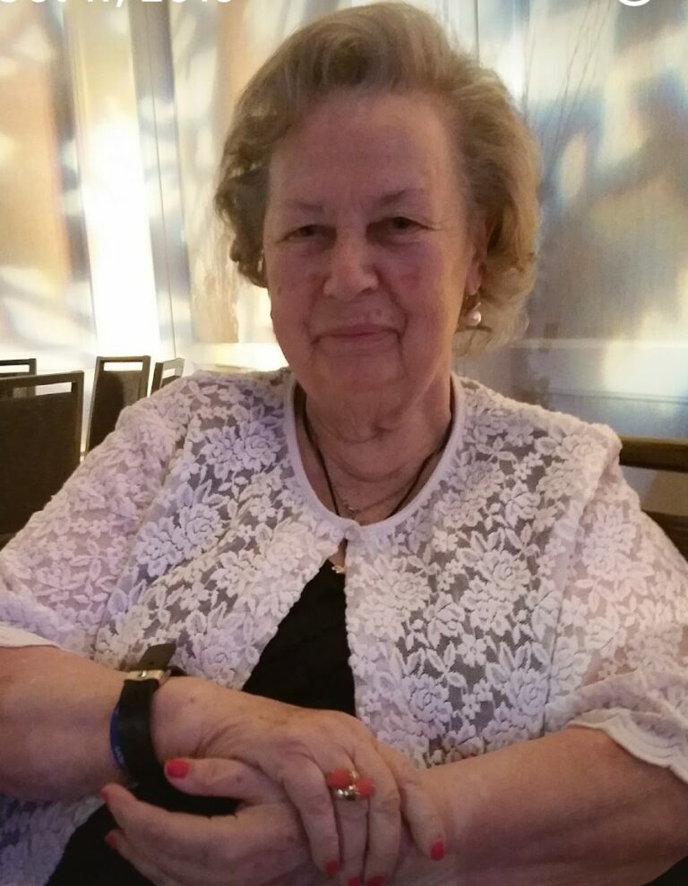 An older woman sitting at a table with a ring on her finger.