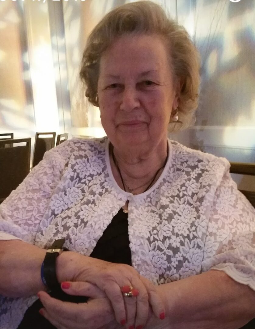 An older woman sitting at a table with a ring on her finger.