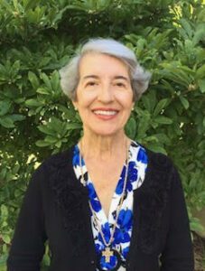 An older woman smiling in front of bushes.