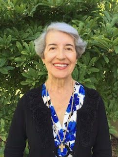 An older woman smiling in front of bushes.