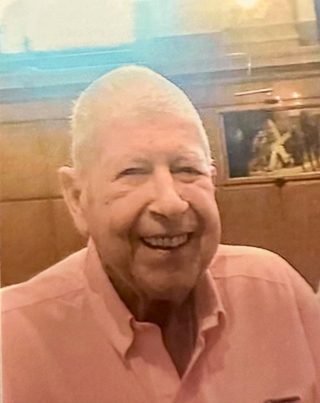 An older man in a pink shirt smiles for the camera.