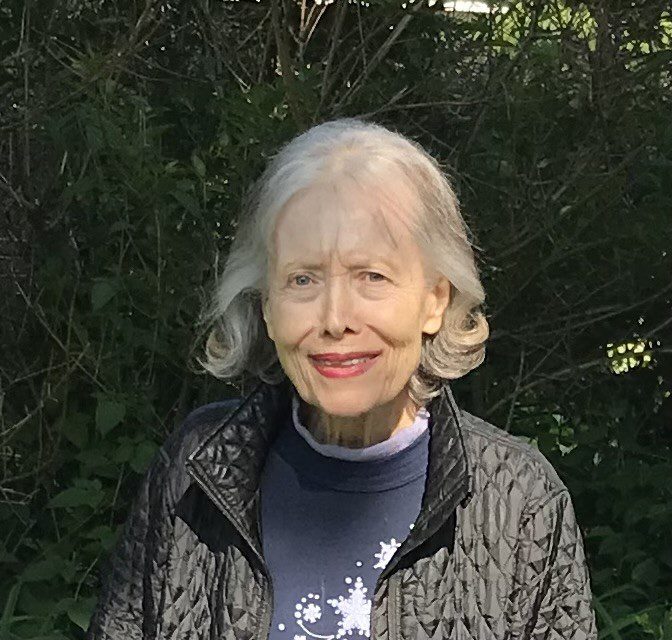 Lilly Kretsos, an older woman standing in front of bushes.