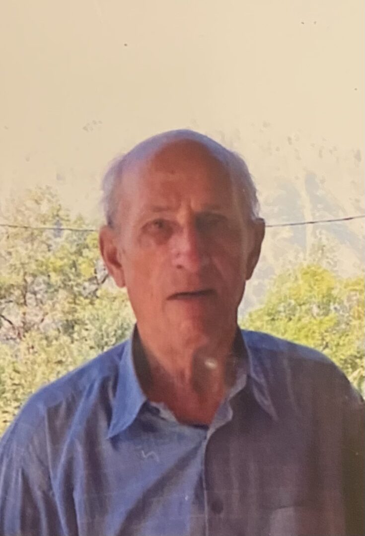An older man in a blue shirt standing in front of a tree.