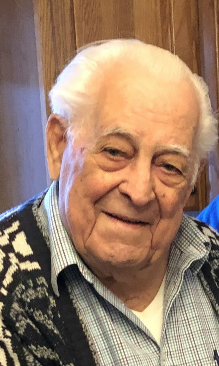 An older man in a sweater smiles for the camera.