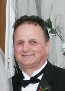 An old man with black color suit smiling at the camera