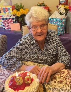 An older woman sitting in front of a cake with candles.
